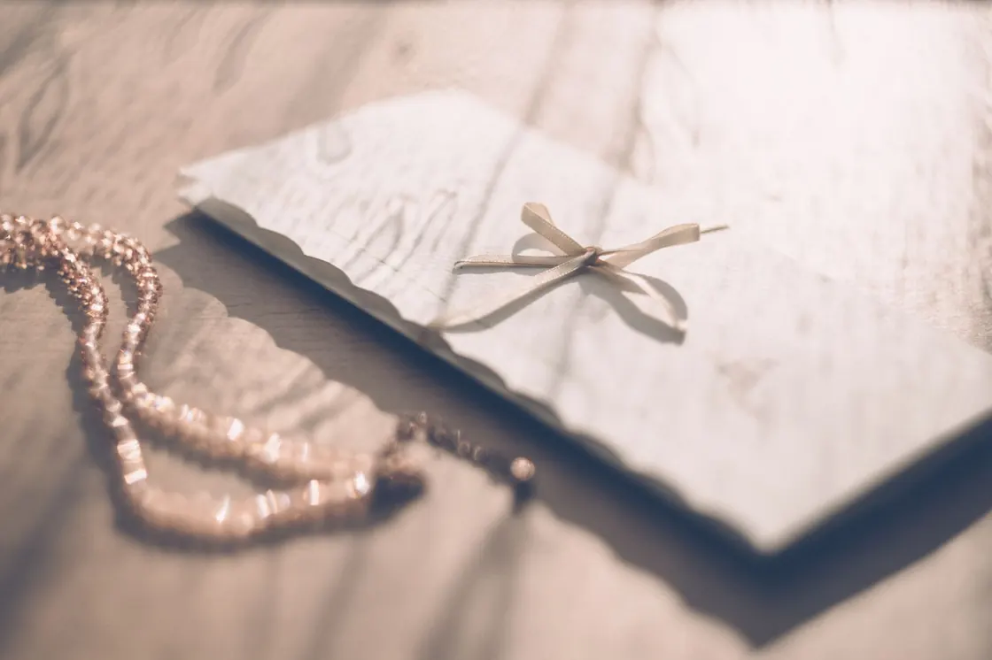 A gift envelope tied with a ribbon resting on a sunlit wooden table