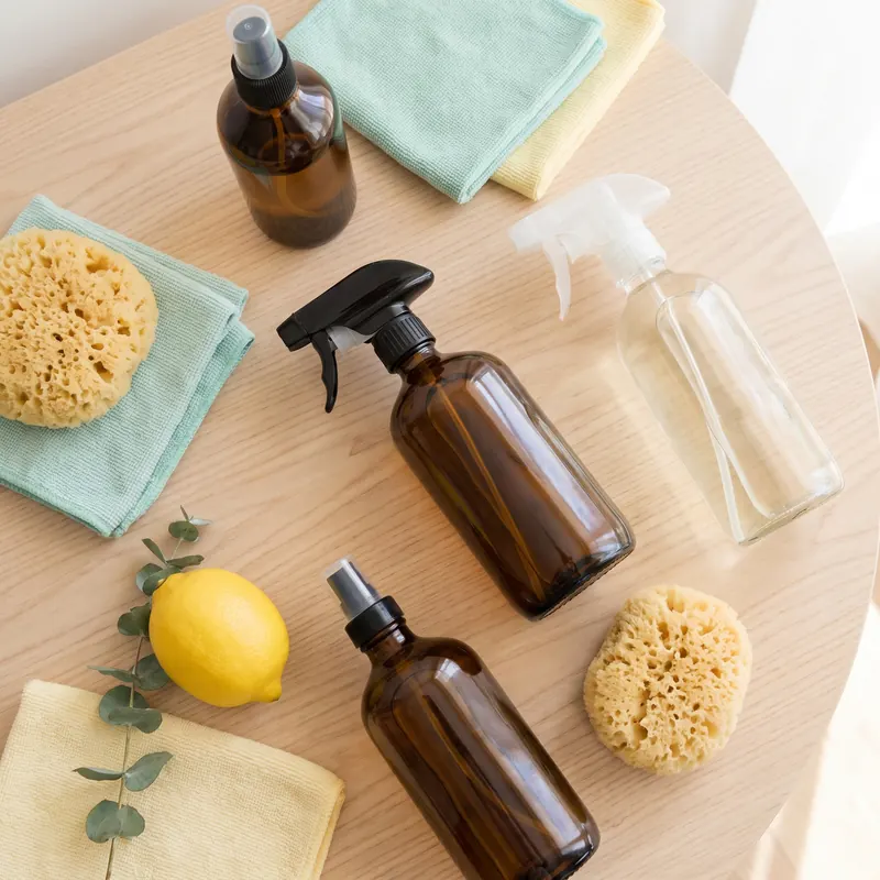 Eco-friendly cleaning supplies, folded cloths and eucalyptus arranged on a pale wooden surface